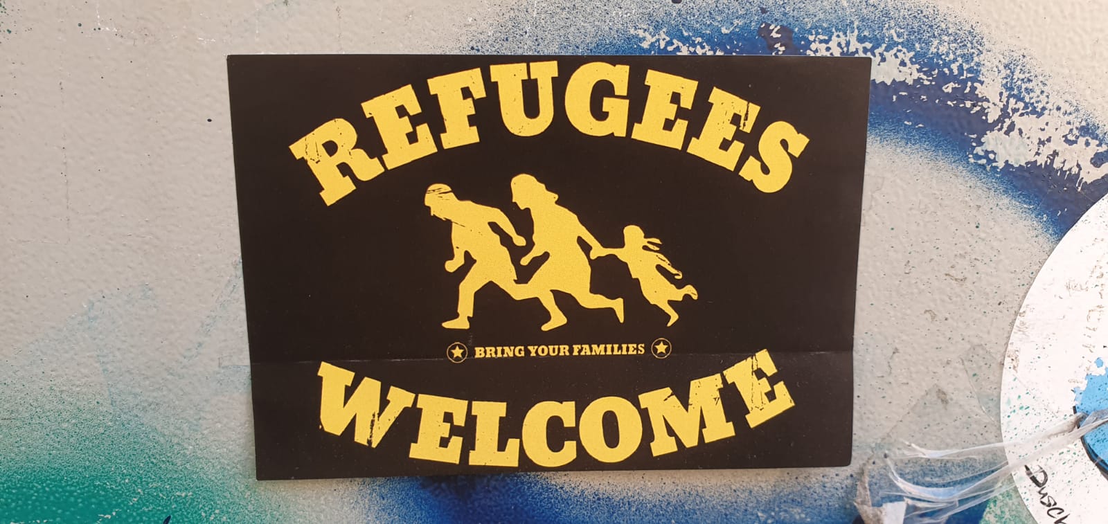 Das Bild zeigt eine fliehende Familie und dazu den Text: Refugees welcome, als Flüchtlinge willkommen.