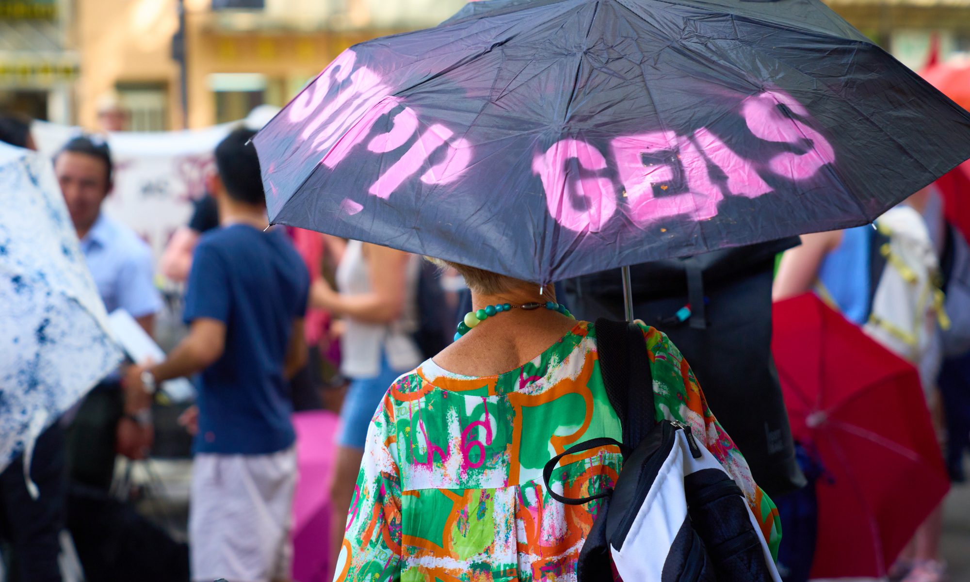 Frau von hinten mit Regenschirm in der Hand. Regenschirm trägt die Aufschrift "Stopp Geas"
