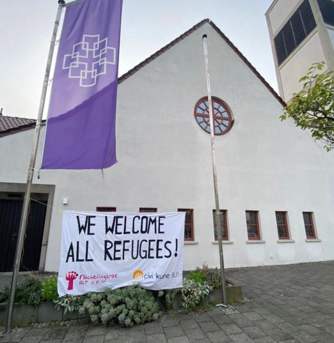 We welcome all refugees - Banner des Flüchtlingsrat RLP e.V. vor einer Kirche in Darmstadt