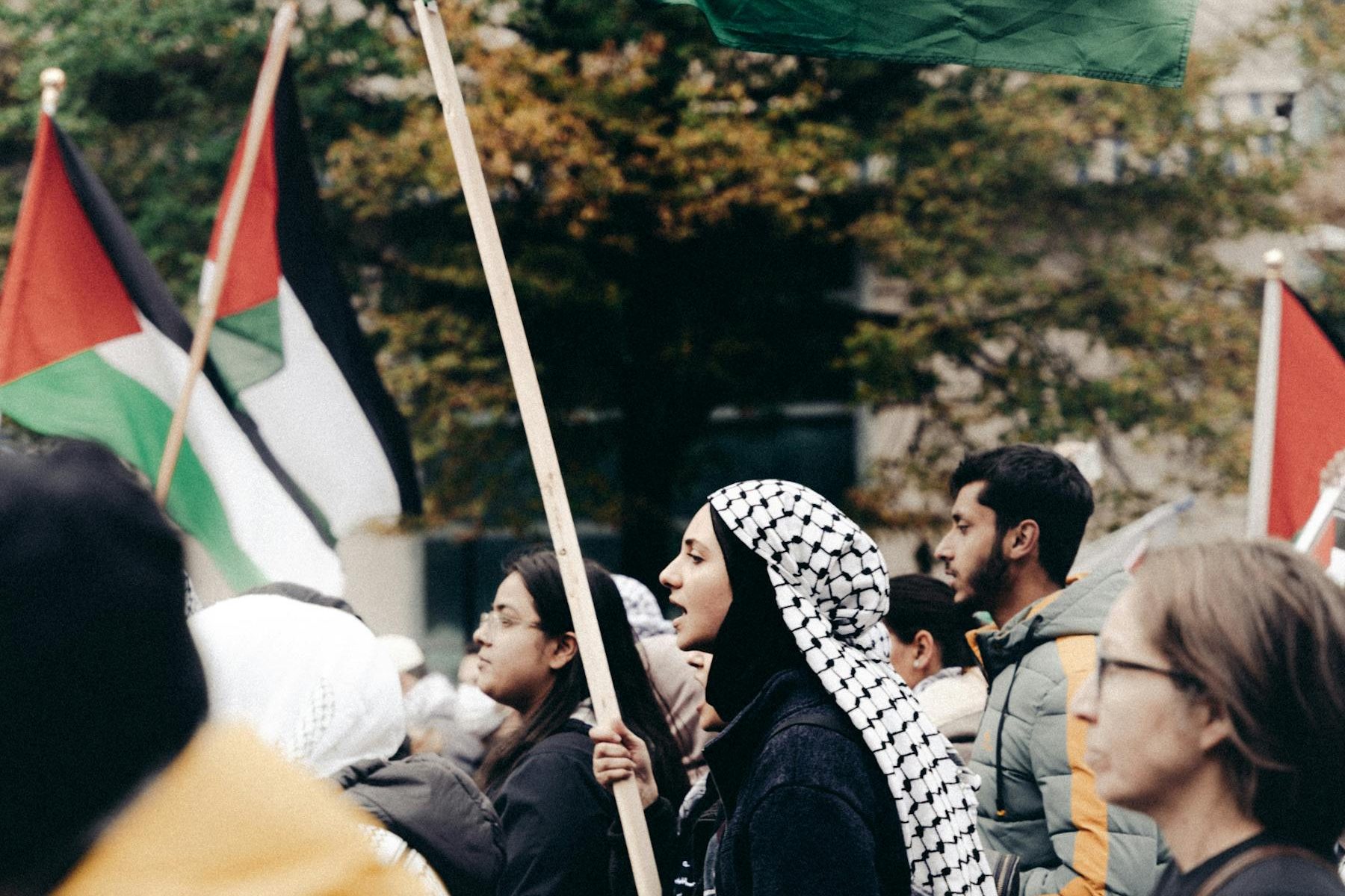 Eine Frau in Abbaya und mit Kuffiyeh trägt auf einer Demonstration einen Palästinafahne